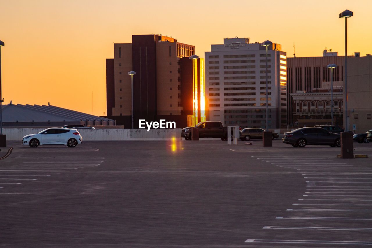 Cars on street by buildings against sky during sunset