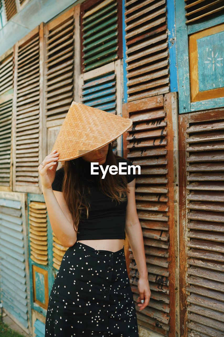 Woman wearing hat while standing by wooden wall