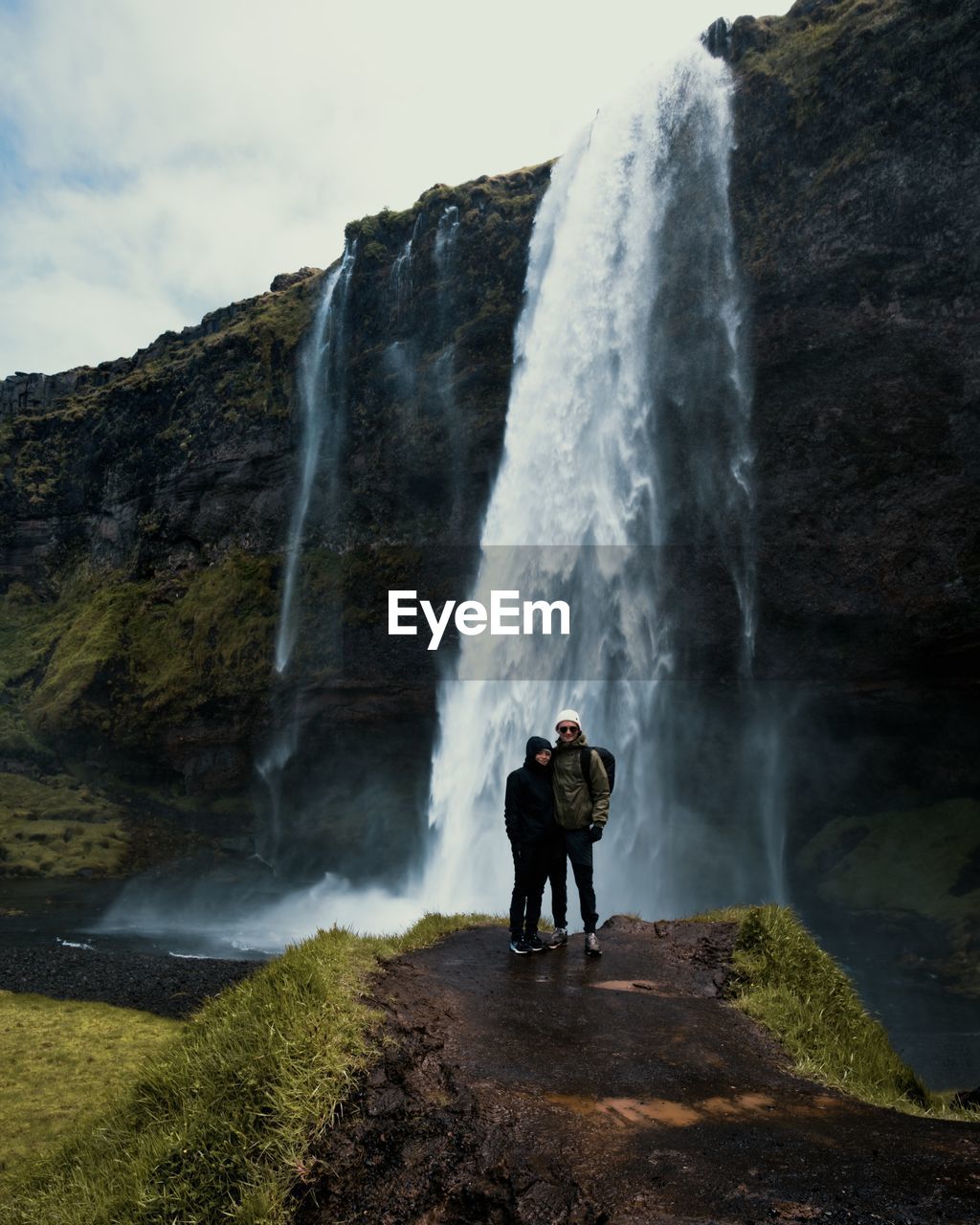 Rear view of couple standing against waterfall iceland