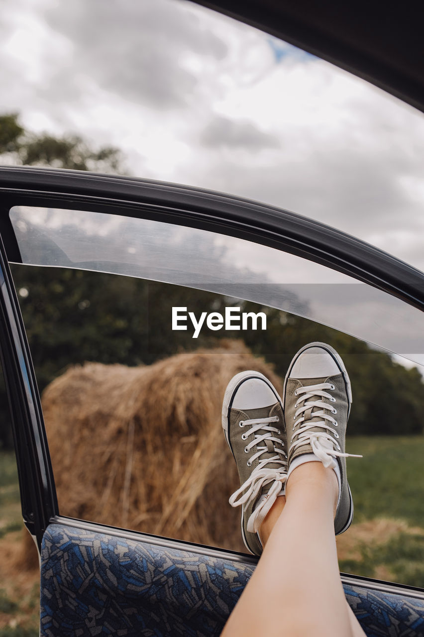 Legs in stylish marsh-colored sneakers in car window, view of an autumn field with haystacks. 