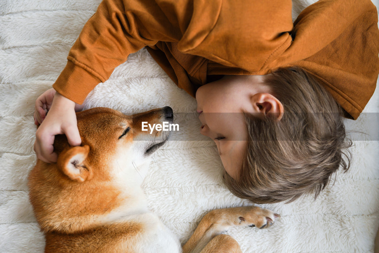 View from above on cute boy and his domestic ginger dog are lying on a bed waiting for christmas