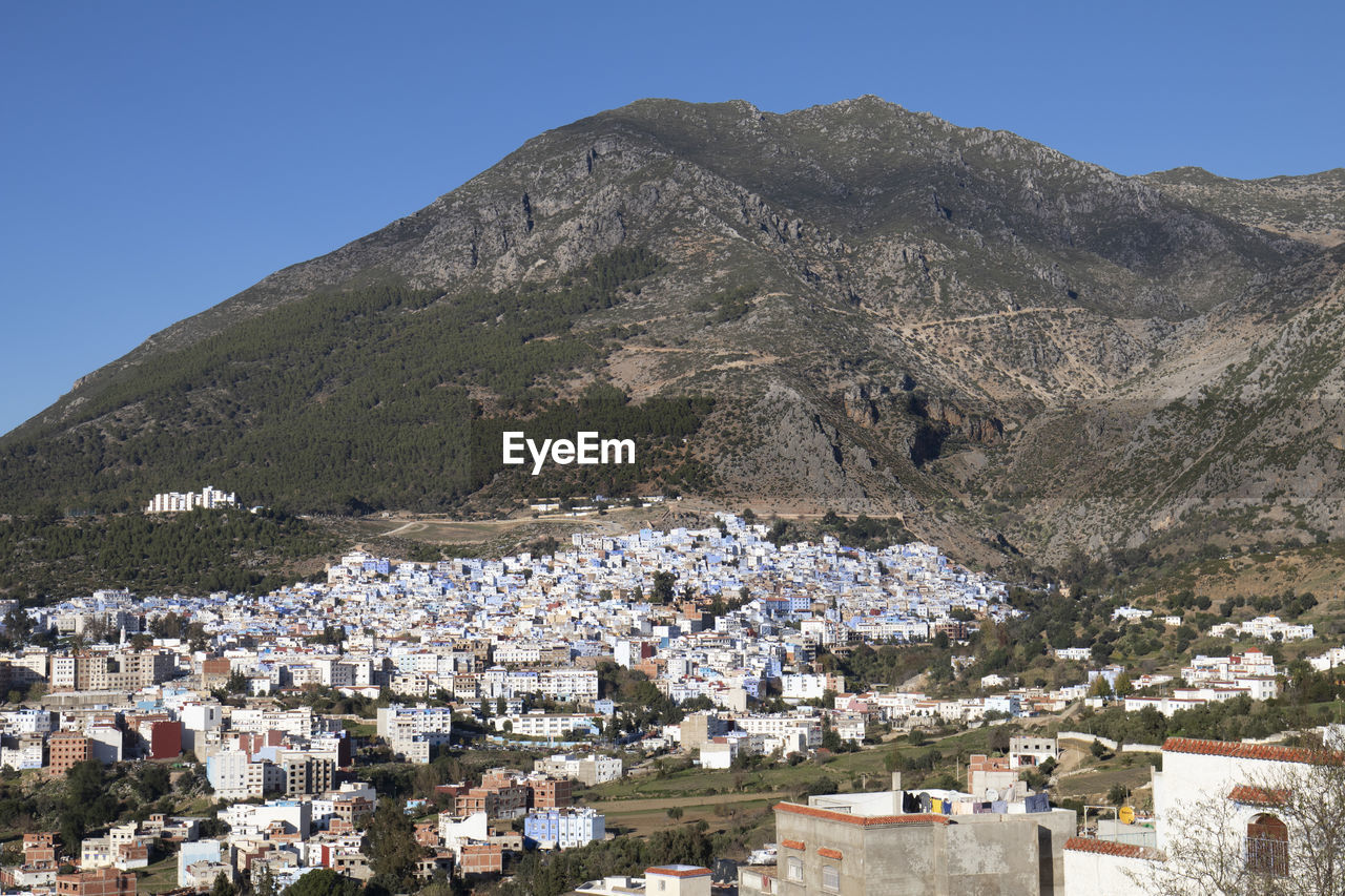 Aerial view of townscape and mountains against clear blue sky