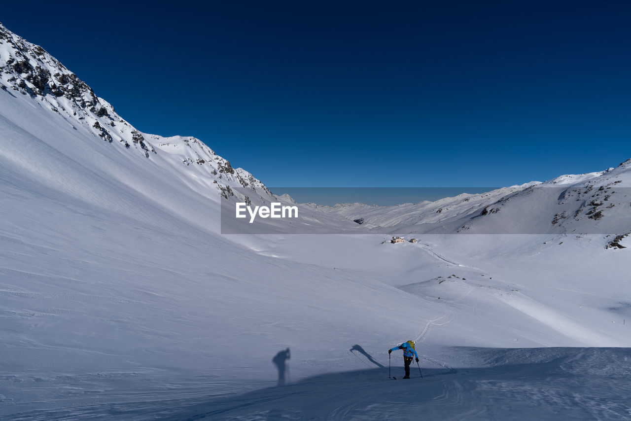 Person hiking on snowcapped mountains against clear blue sky
