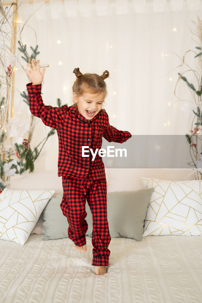 Cute little girl in red christmas pajama jumping on bed, having fun
