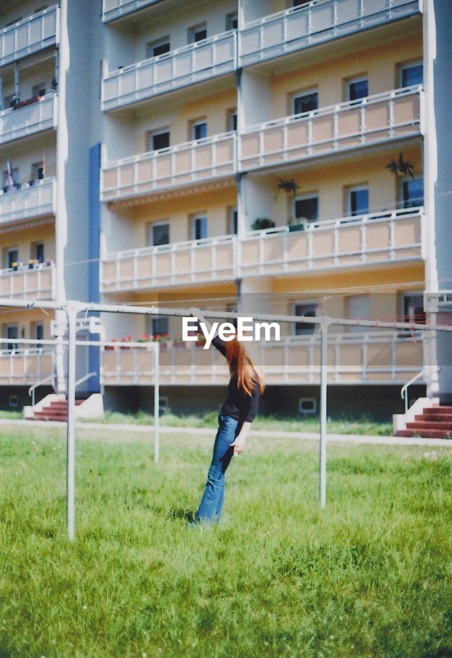 Full length of woman leaning on metallic pole against building