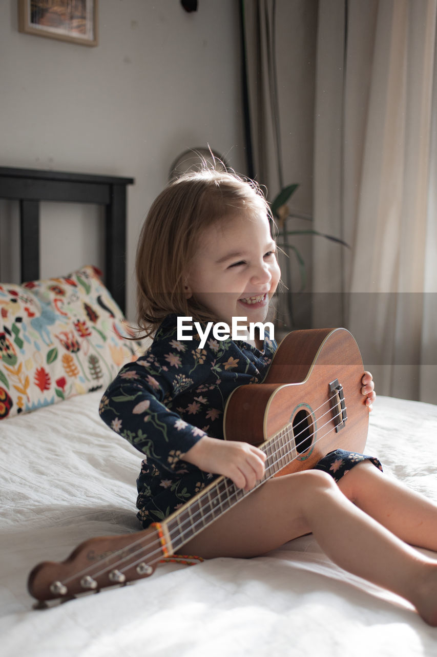 Happy girl playing guitar on bed at home