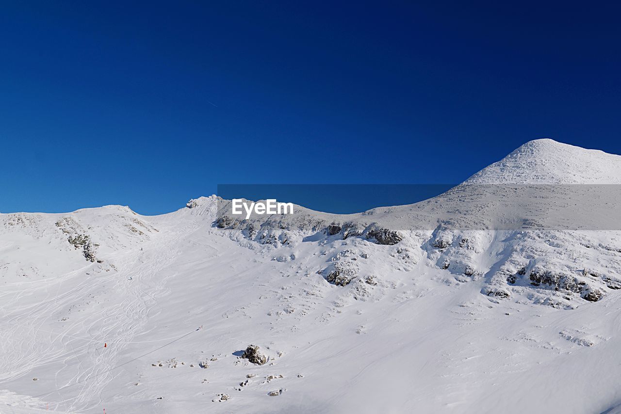 Scenic view of snowcapped mountains against clear blue sky