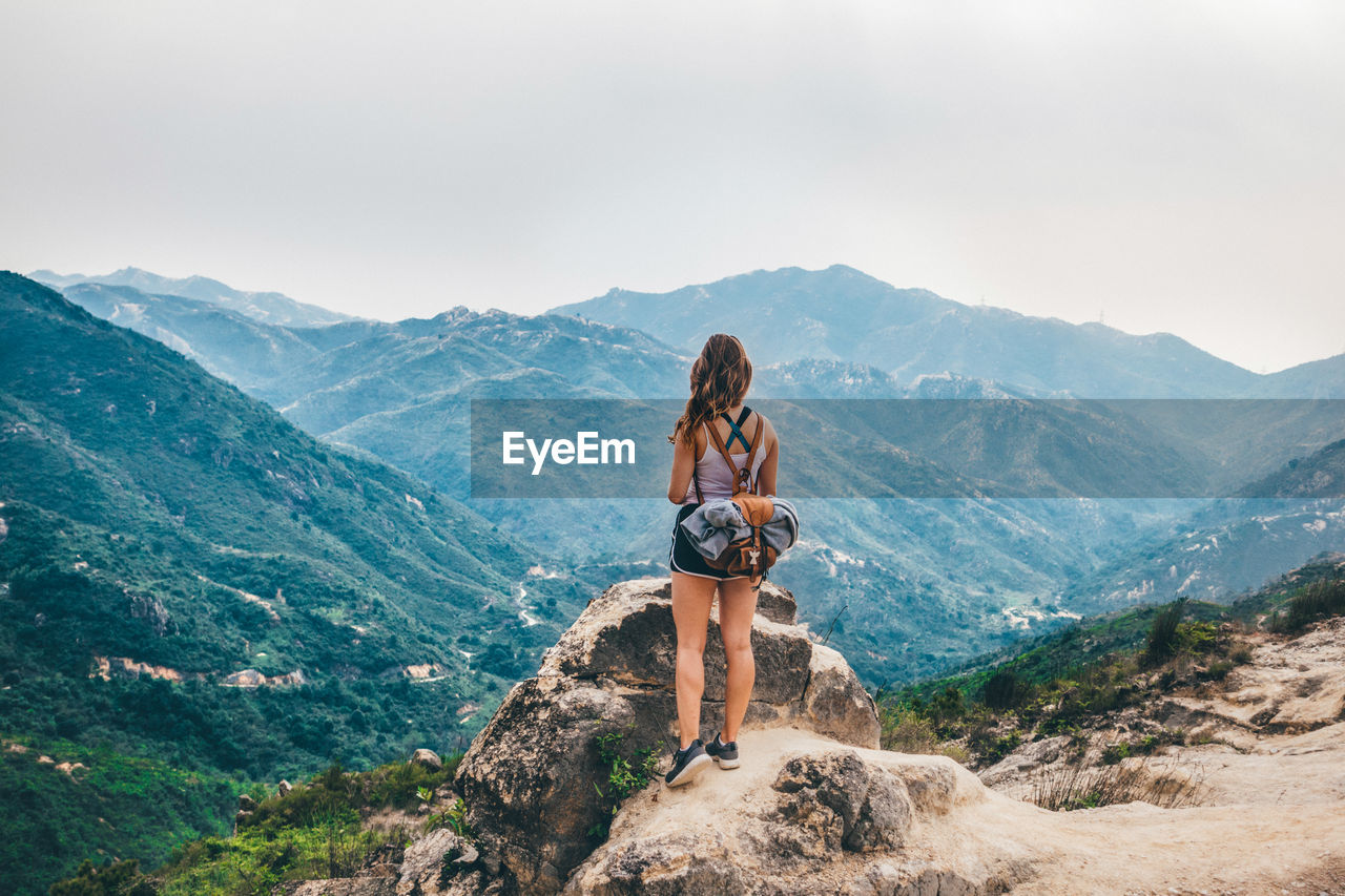 WOMAN WITH ARMS OUTSTRETCHED AGAINST MOUNTAINS AGAINST SKY