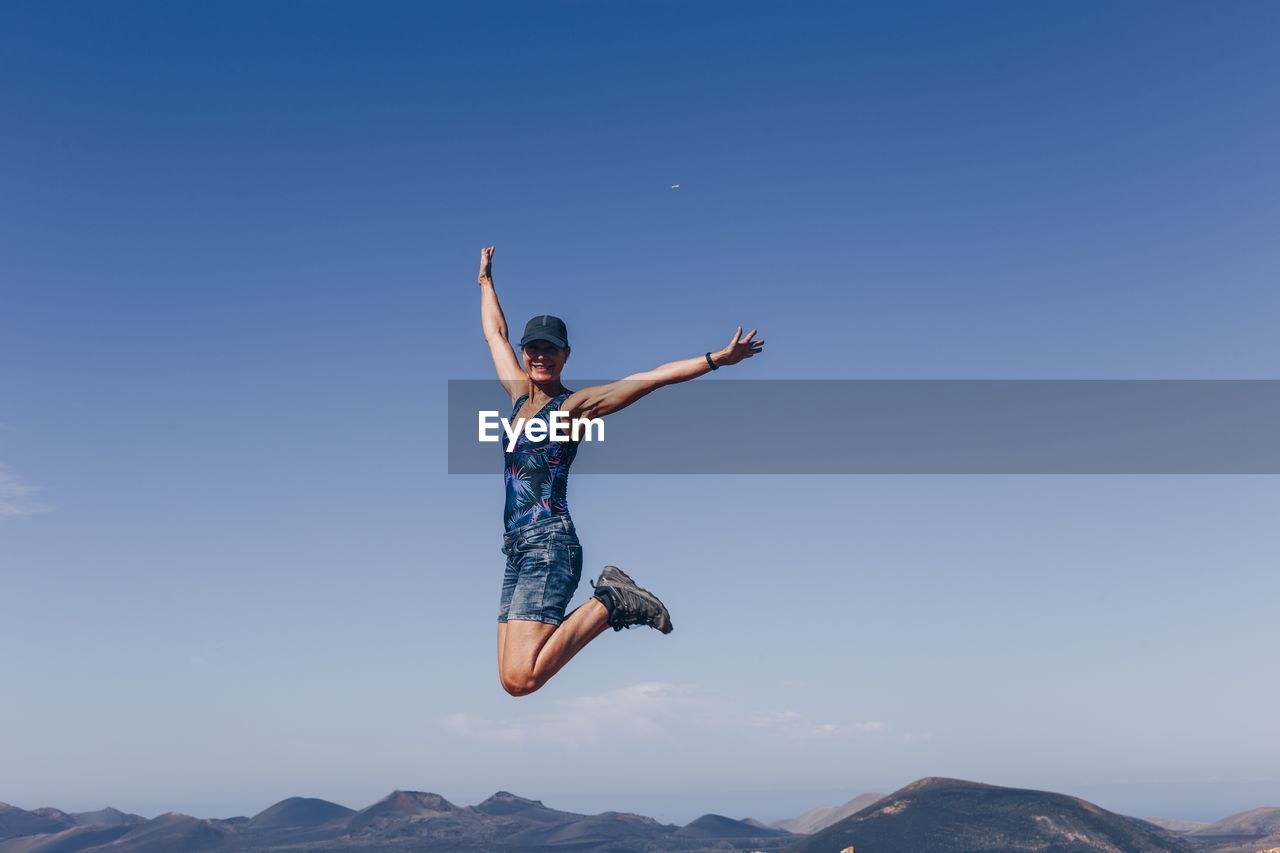 Low angle view of person jumping against blue sky