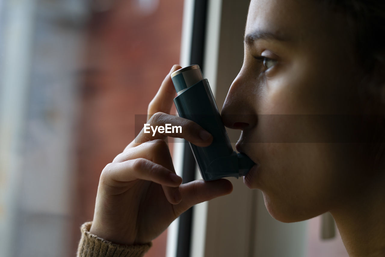 Young woman taking the blue asthma inhaler to treat an asthma attack.