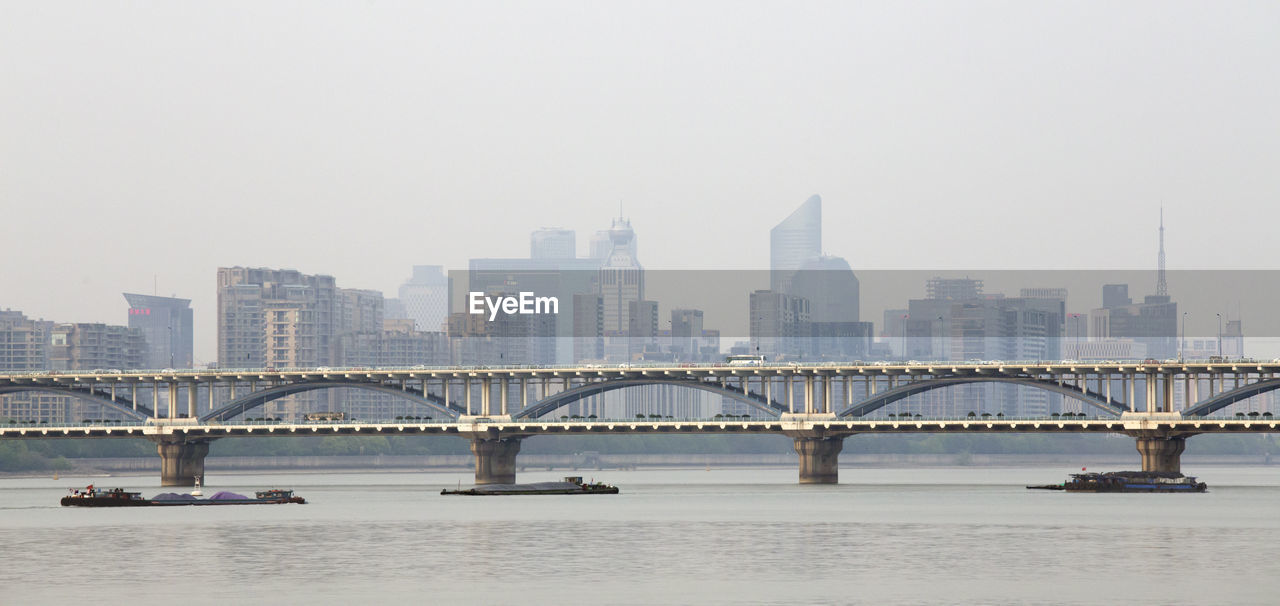 BRIDGE OVER RIVER AGAINST BUILDINGS IN CITY AGAINST CLEAR SKY