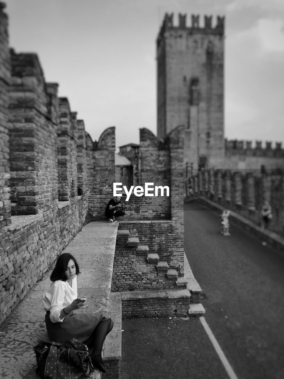 WOMAN SITTING ON WALL OF HISTORICAL BUILDING