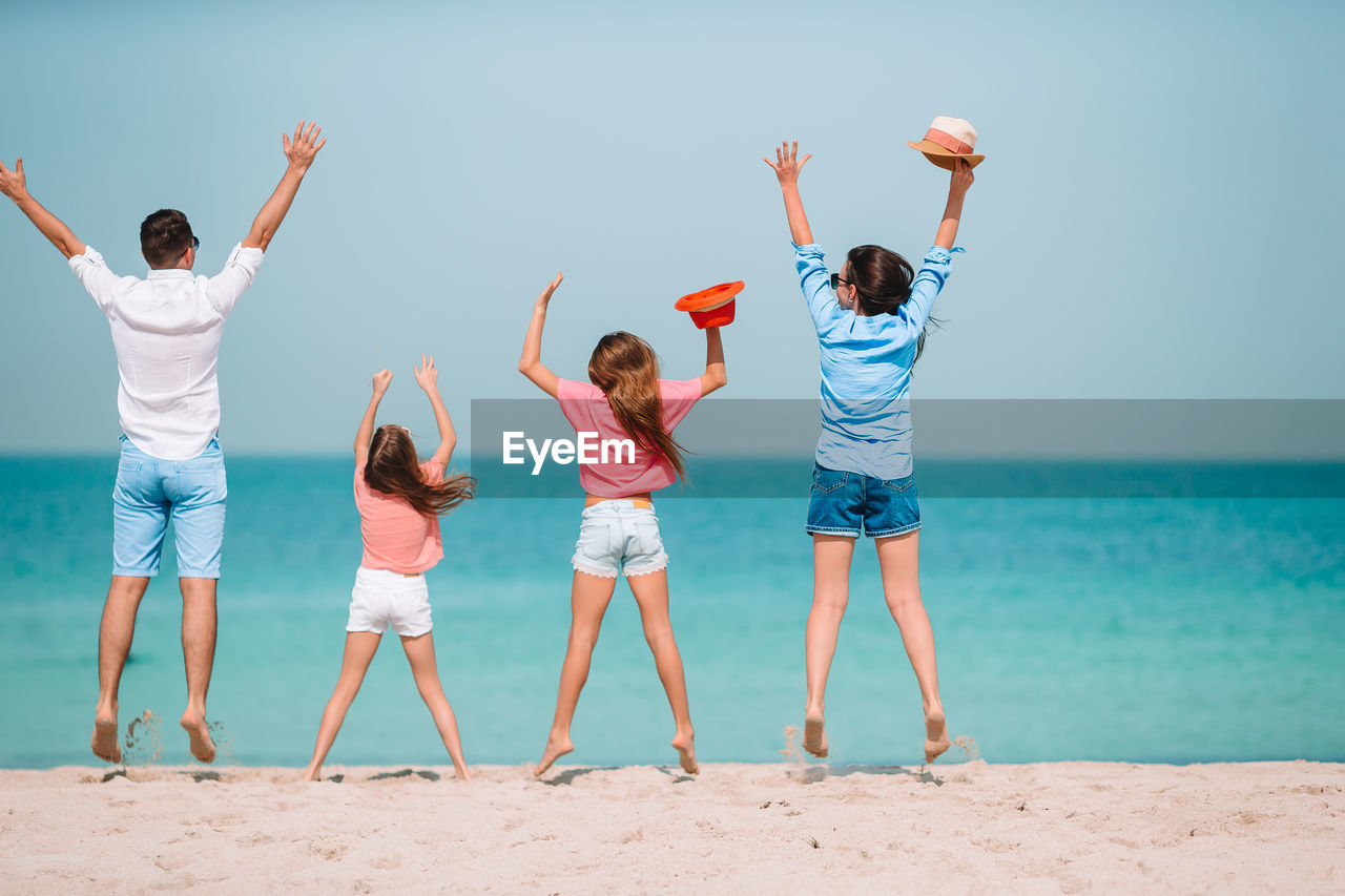 Rear view of friends enjoying at beach against sky