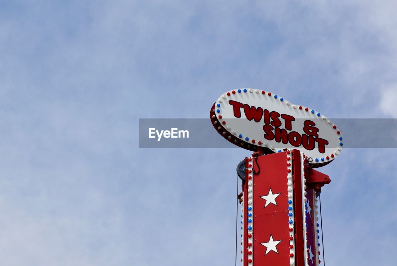 sky, text, communication, low angle view, nature, no people, blue, cloud, red, sign, western script, outdoors, day, amusement park, arts culture and entertainment, architecture, copy space