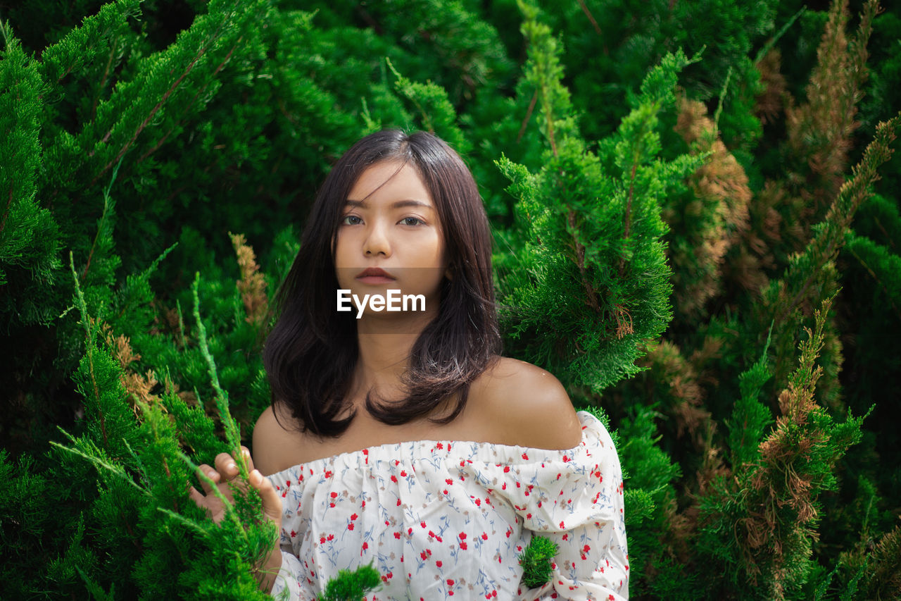 Portrait of beautiful young woman against plants