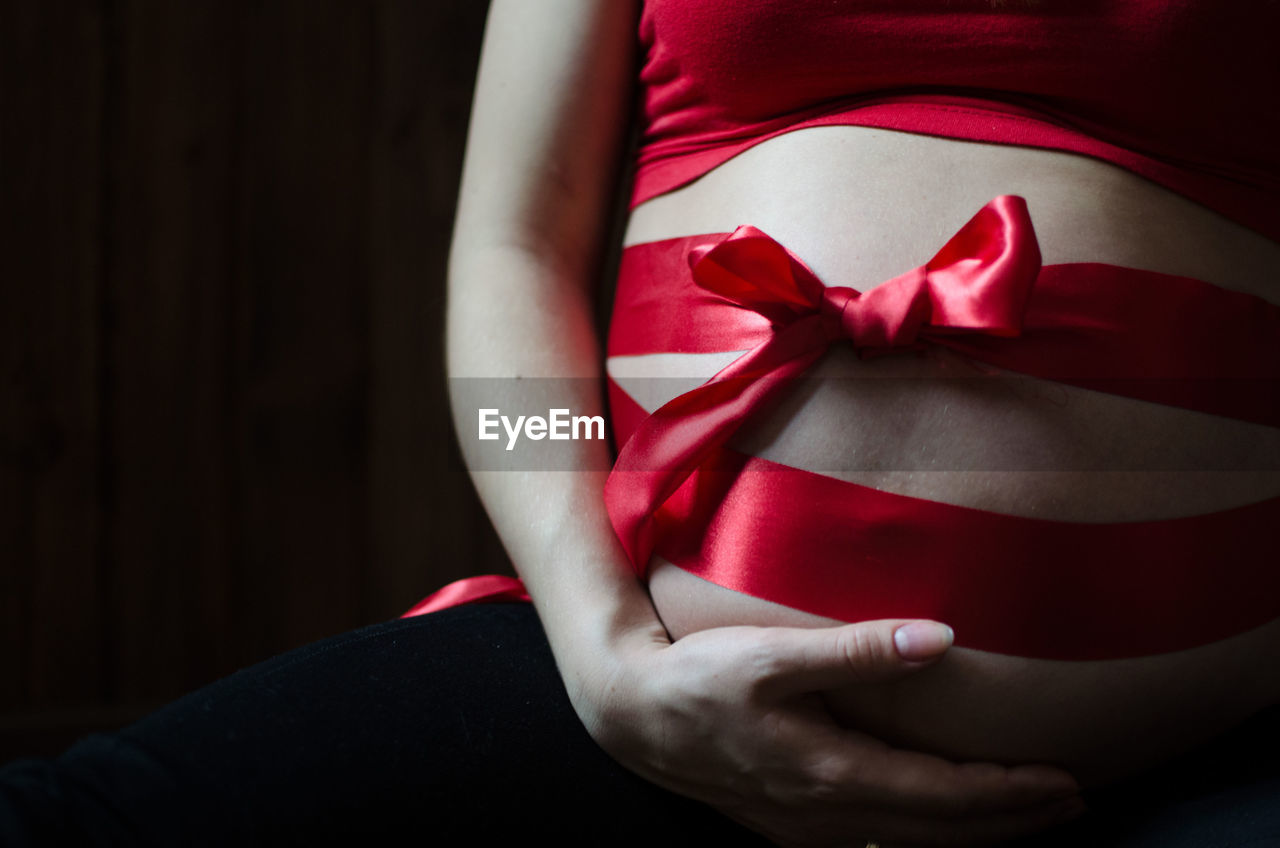 Close-up of pregnant woman with red ribbon tied around belly