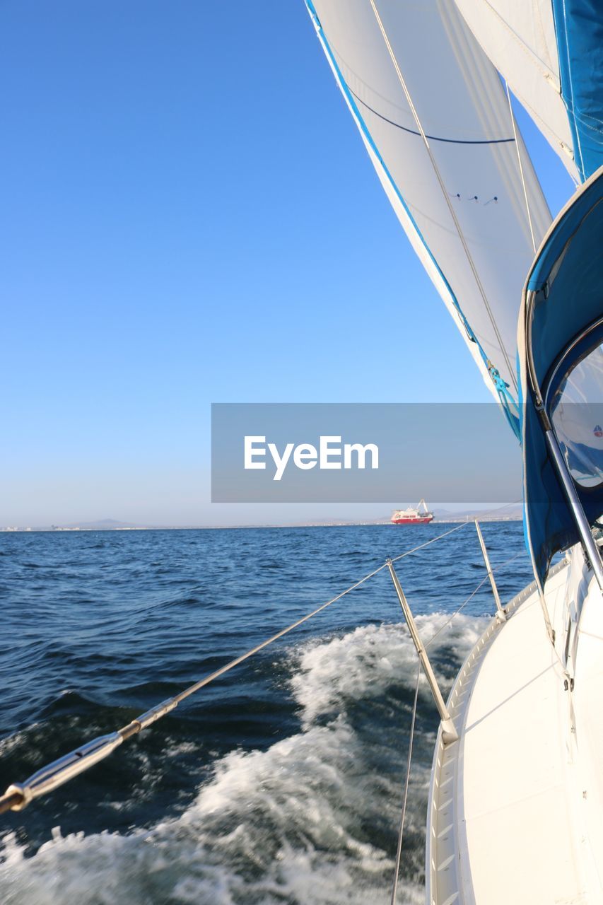 Sailboat sailing in sea against clear blue sky