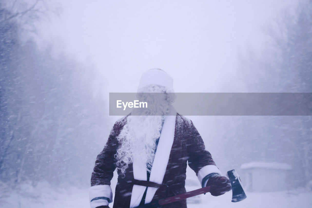 Mid adult man in santa costume standing in forest during winter