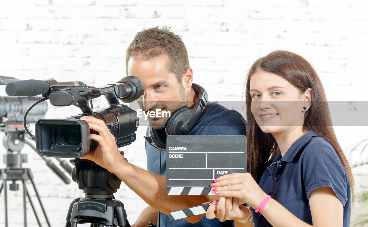 People with digital video camera standing against wall