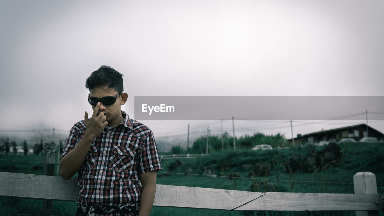 Man wearing sunglasses standing by railing against sky