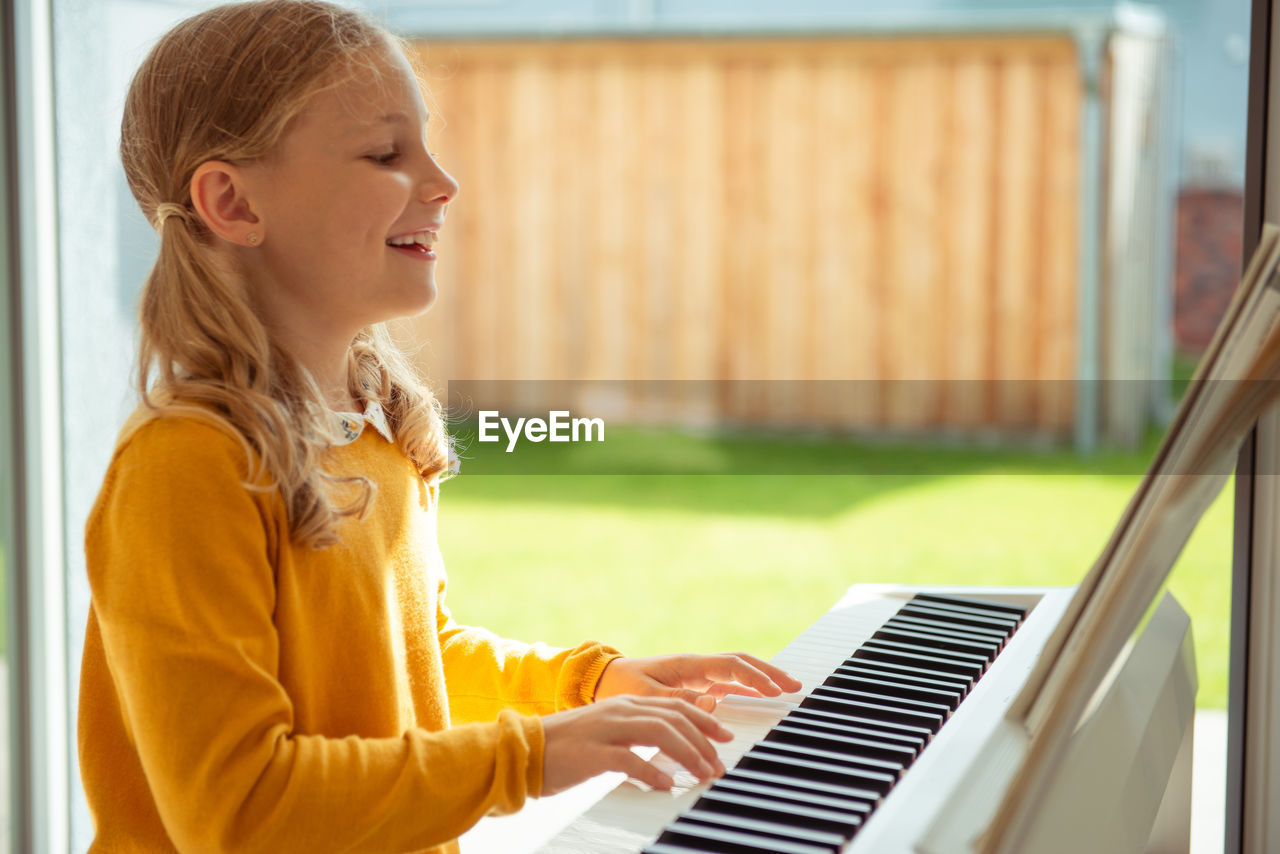 Side view of smiling girl playing piano at home