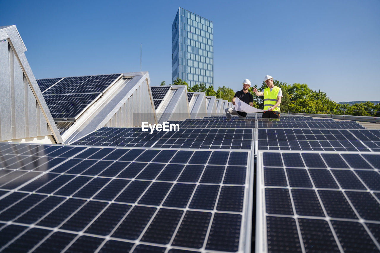 Two technicians strategizing on the rooftop of a corporate building equipped with solar panels