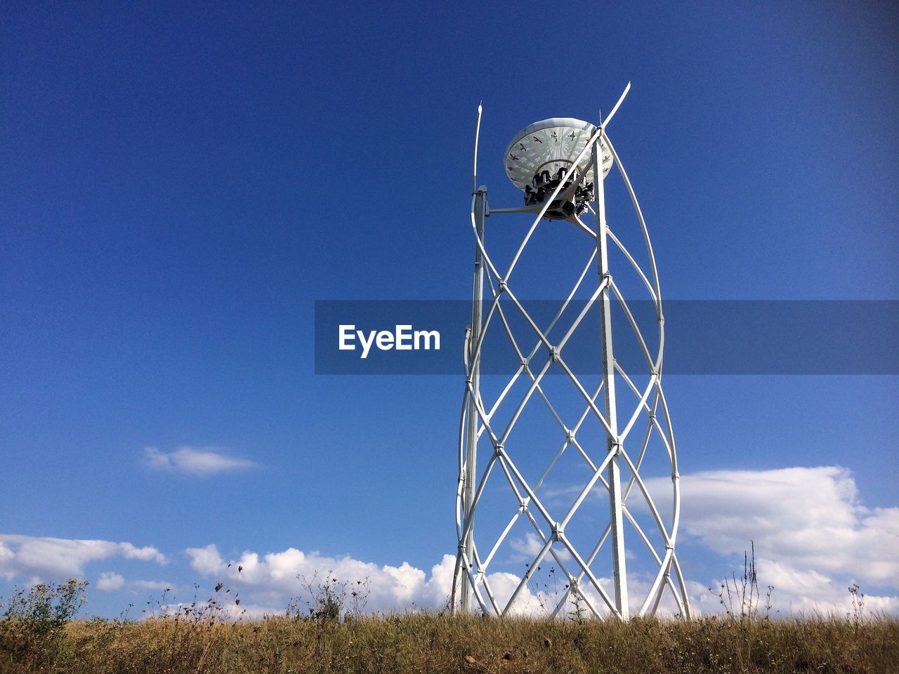 Low angle view of ferris wheel on field against blue sky