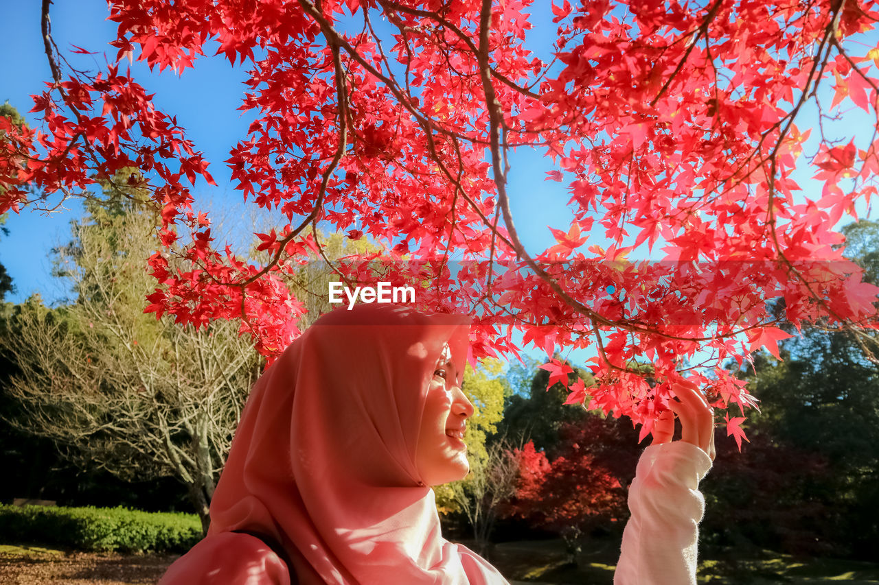 Side view of woman with red flowers against trees