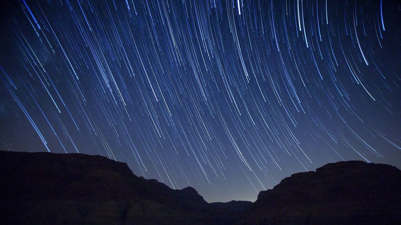 Star trails over silhouette mountains at night