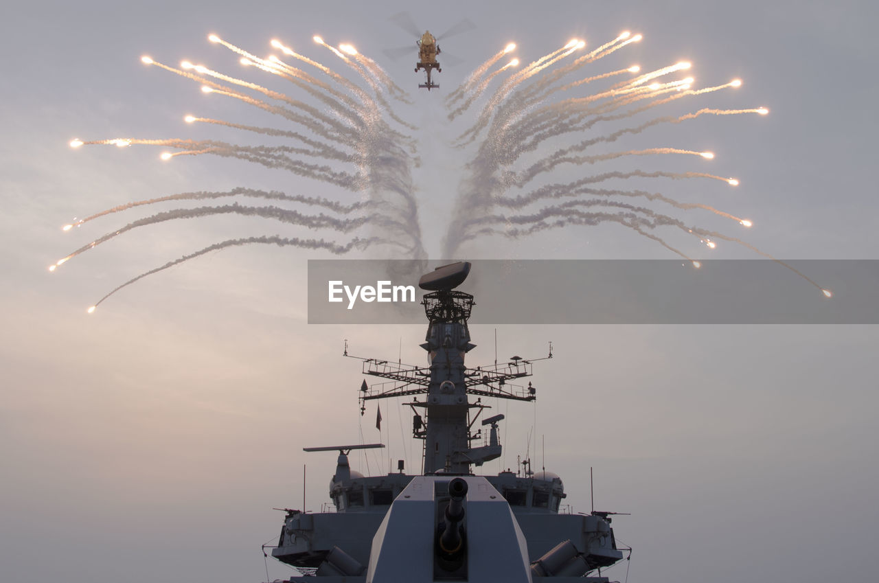 Low angle view of fireworks display over ship by helicopter in sky 