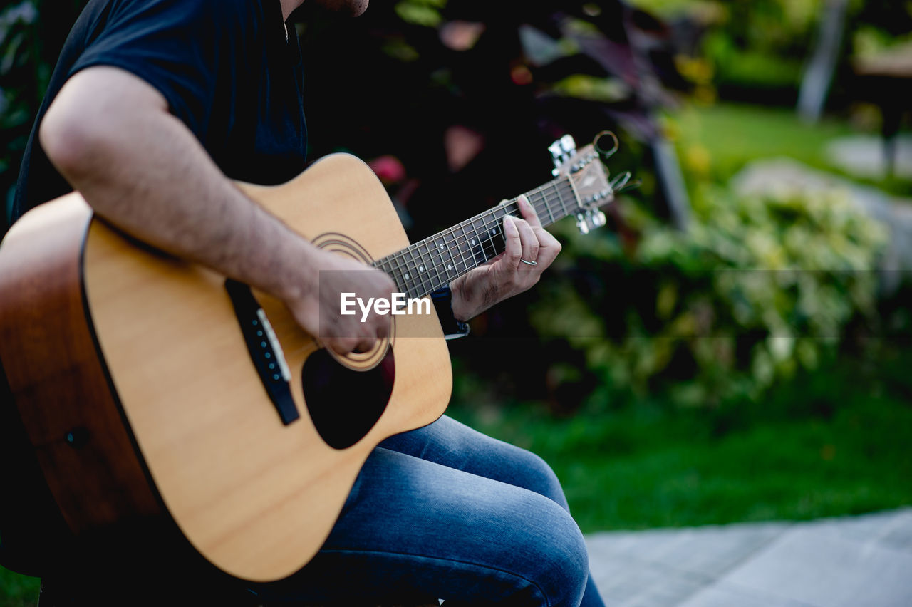 Midsection of man playing guitar outdoors