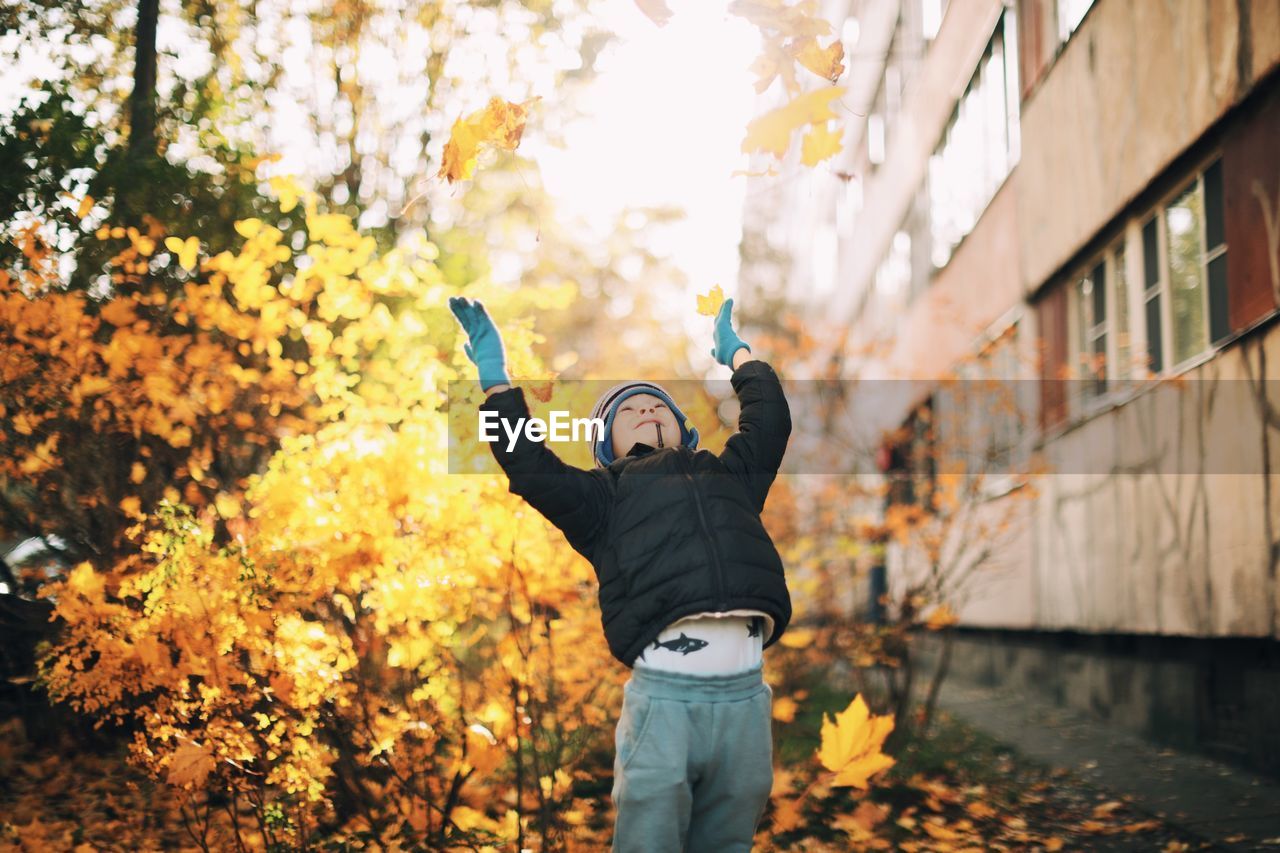 Cute boy throwing dry leaves during autumn