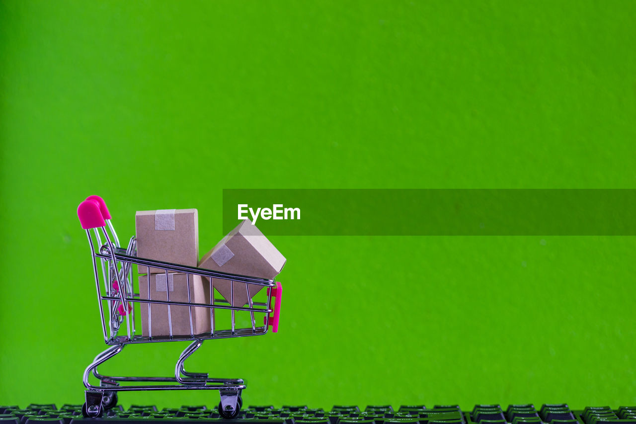 Close-up of small shopping cart with packages on keyboard against green wall