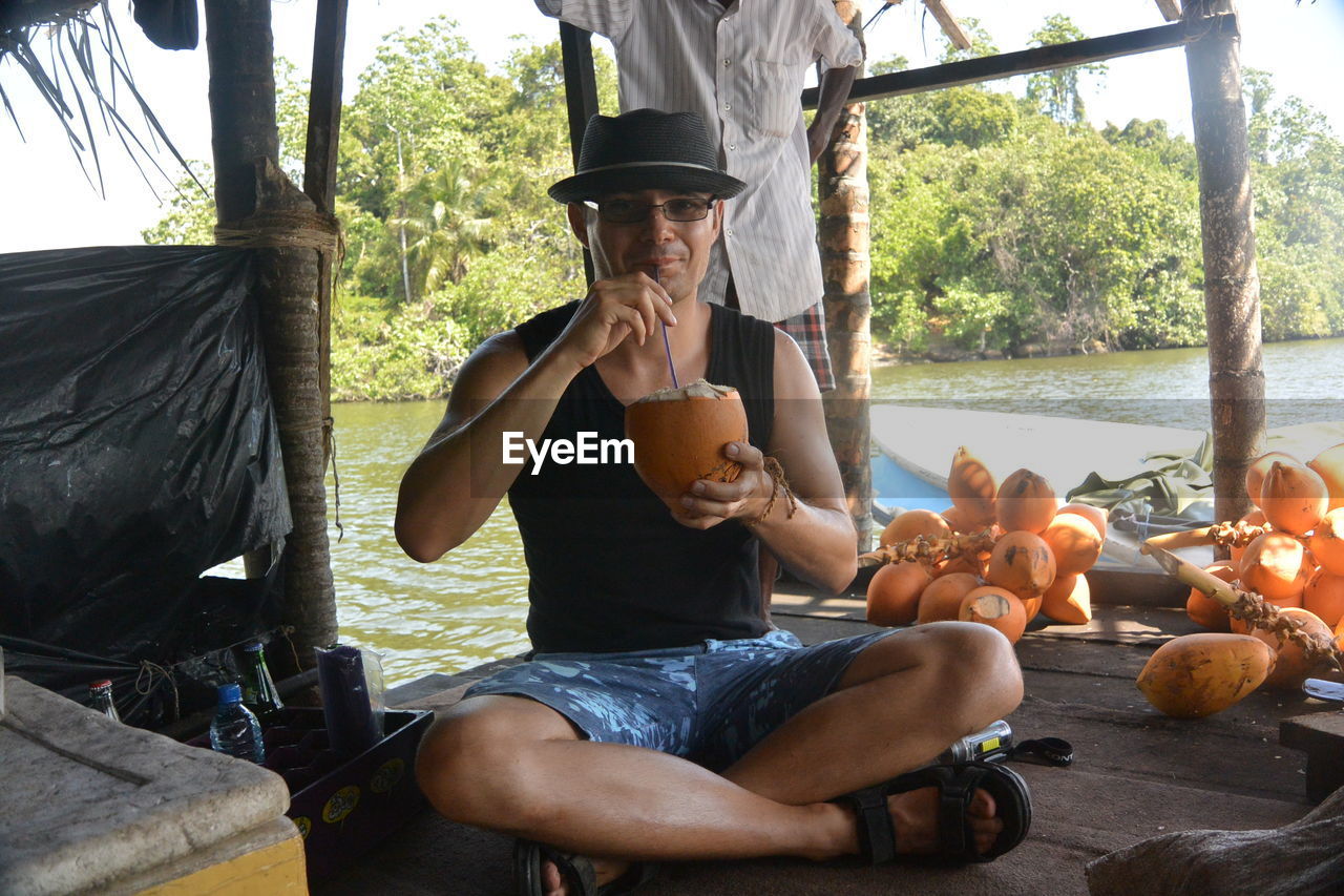 Portrait of man drinking coconut water while sitting on boat in river