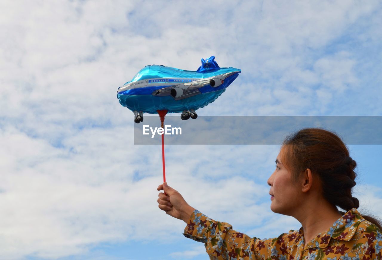 Low angle view of woman holding balloon against sky
