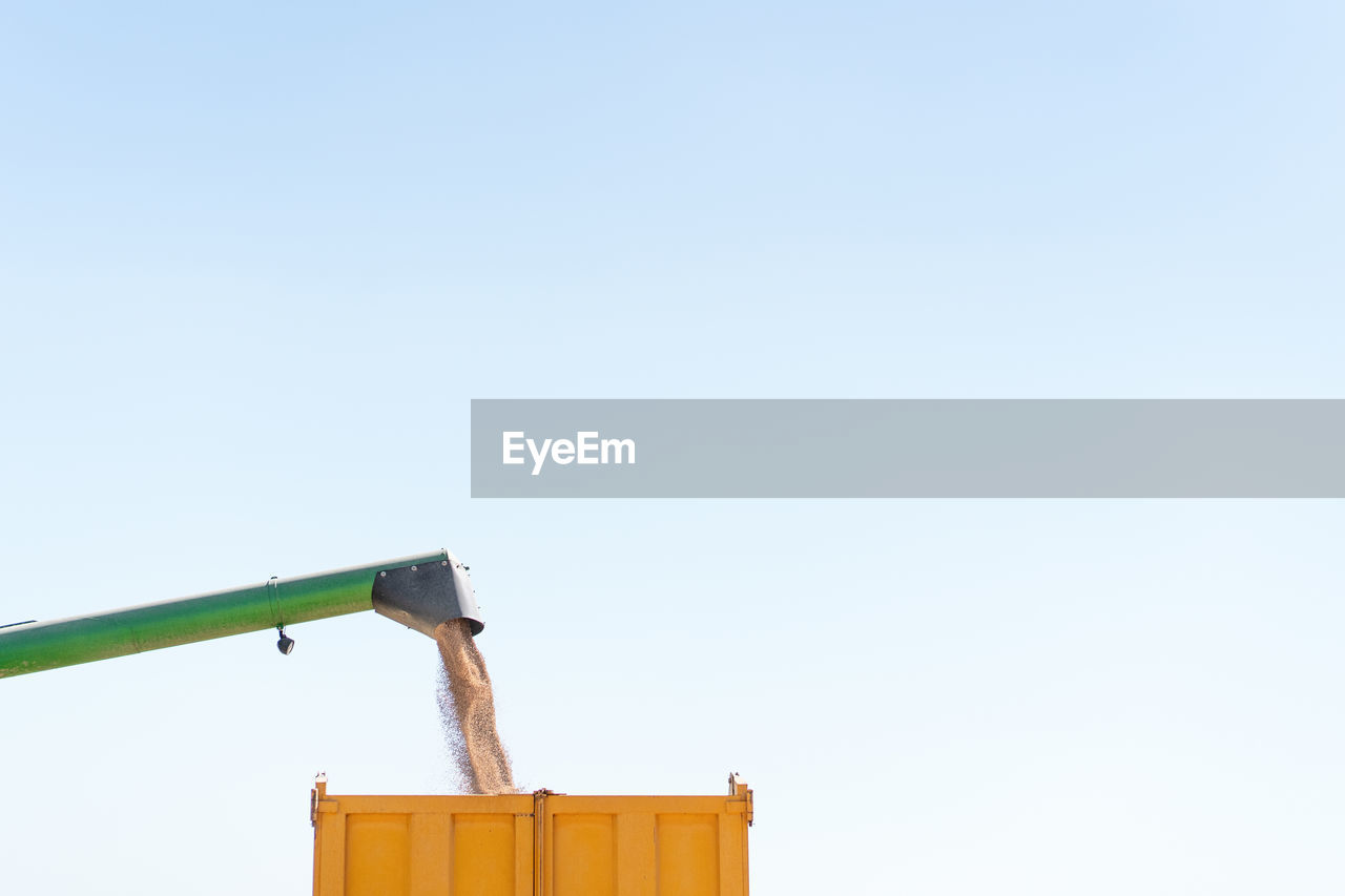 Low angle of detail of combine harvester pouring wheat grain in trailer while working in agricultural field in countryside