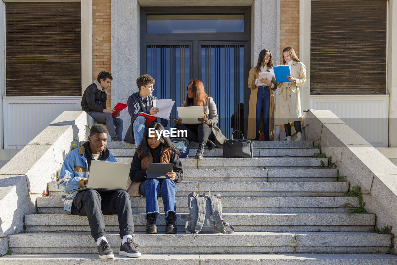 Friends studying over tablet pc and laptop on steps on campus