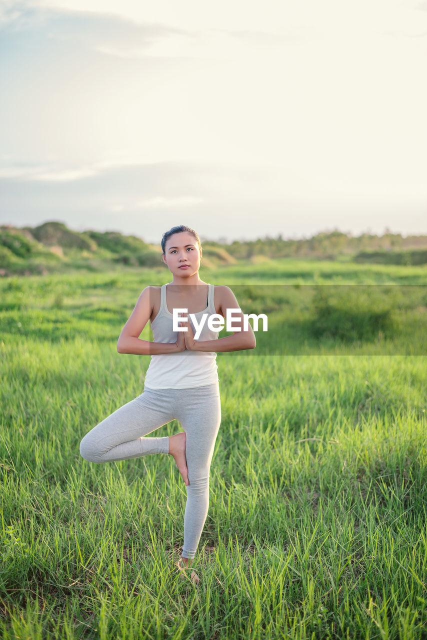 Young woman practicing yoga on grassy field