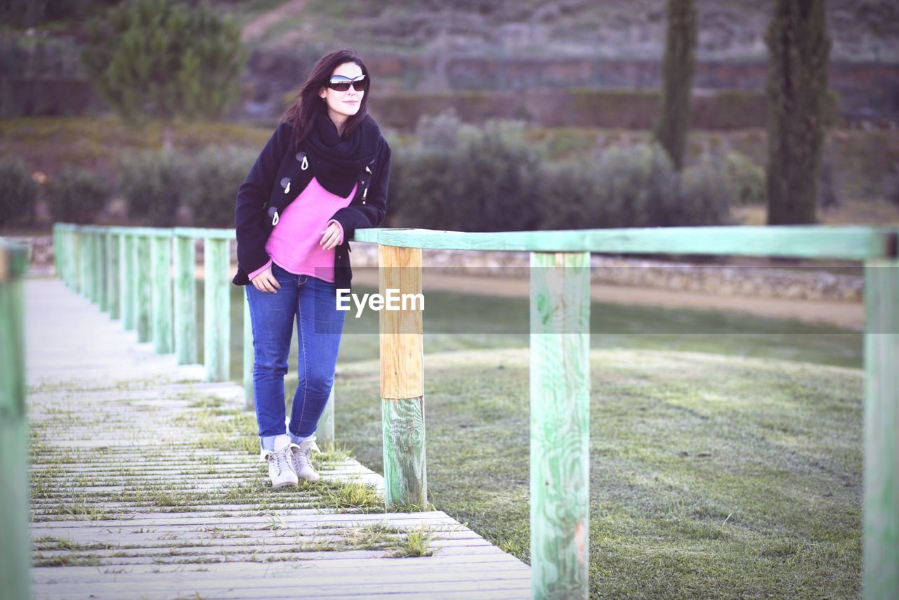 Full length of young woman standing at footbridge on field