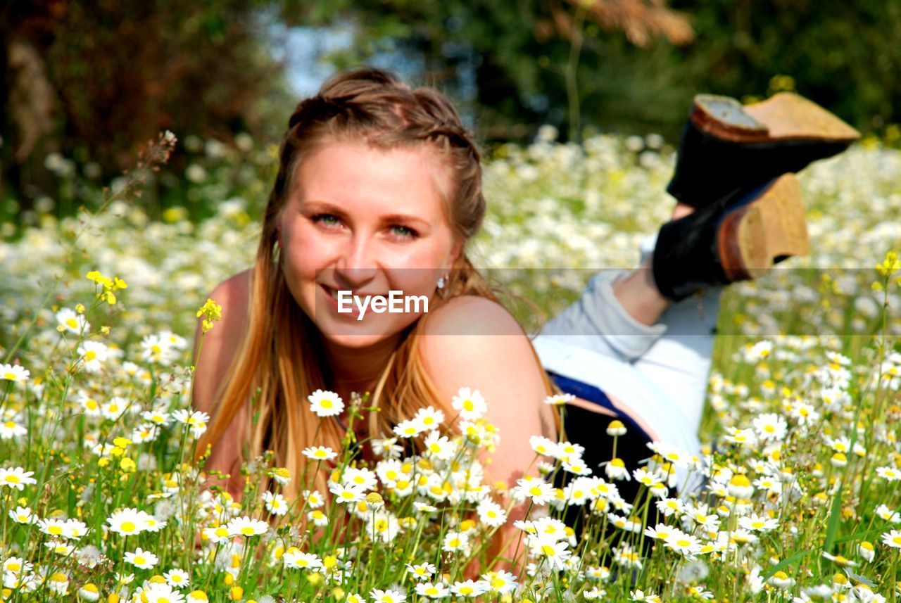 PORTRAIT OF SMILING WOMAN WITH FLOWERS ON PLANT