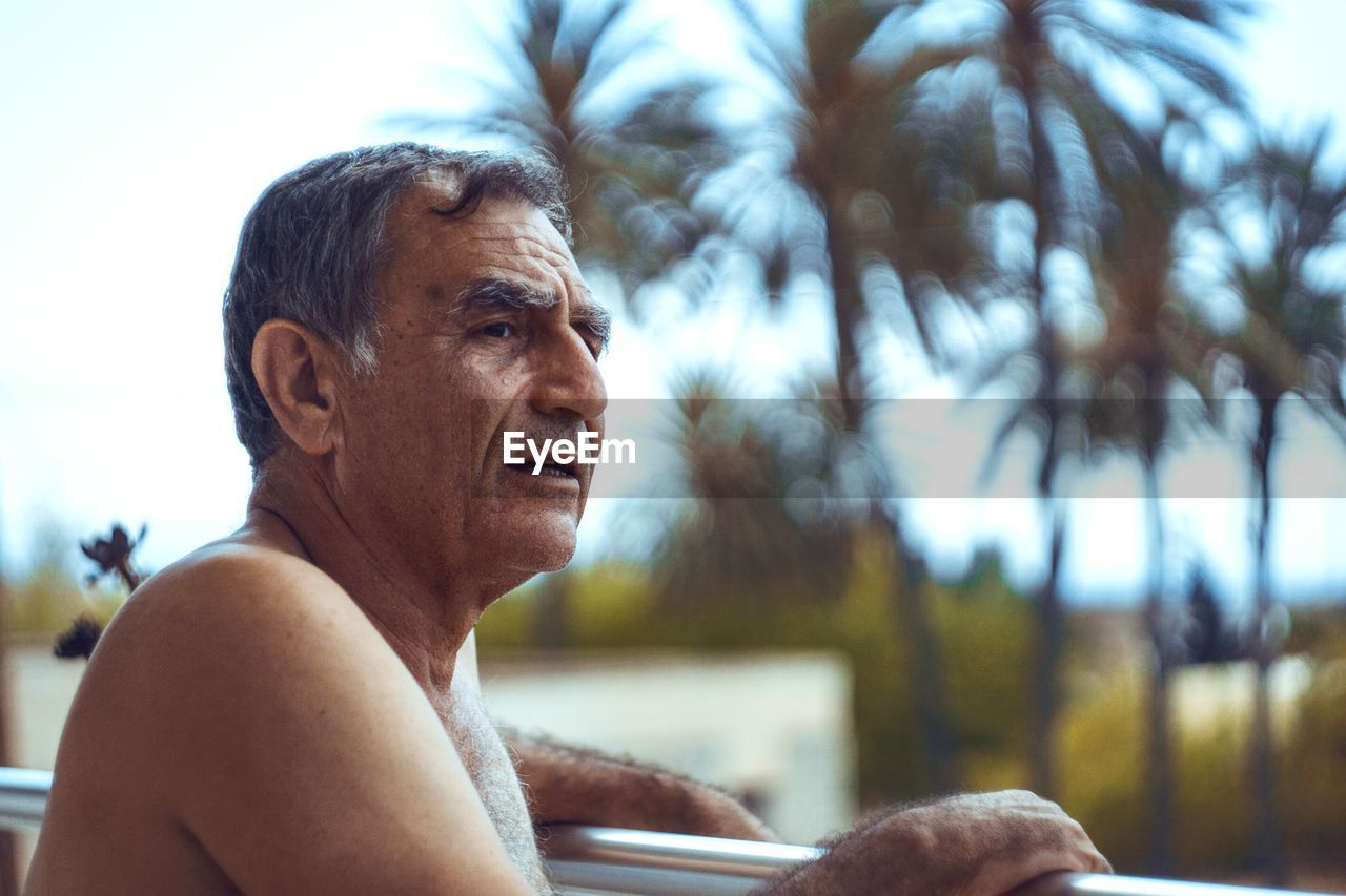 Shirtless senior man standing by railing at balcony