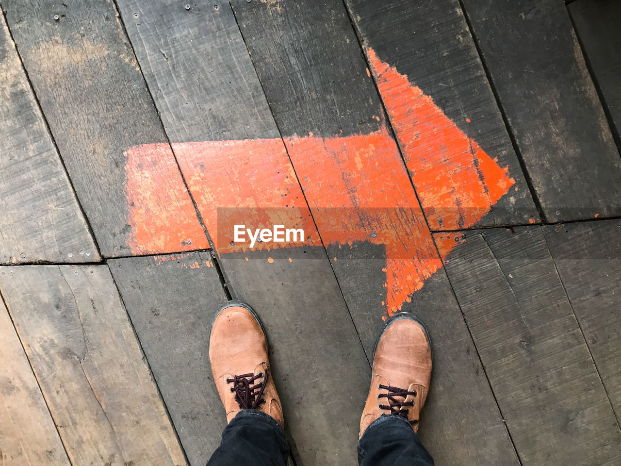 Low section of man standing on orange arrow sign on floorboard