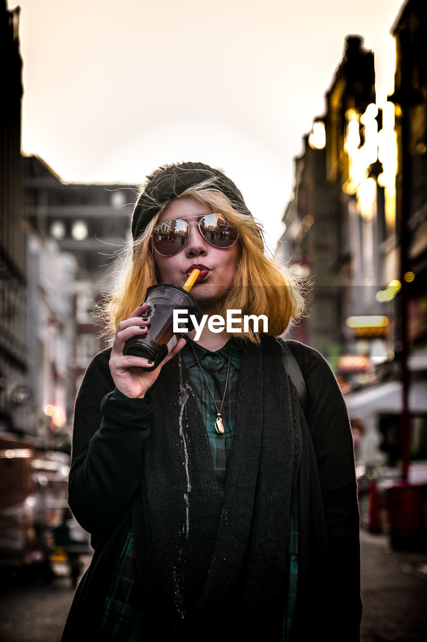 PORTRAIT OF YOUNG WOMAN STANDING IN CITY