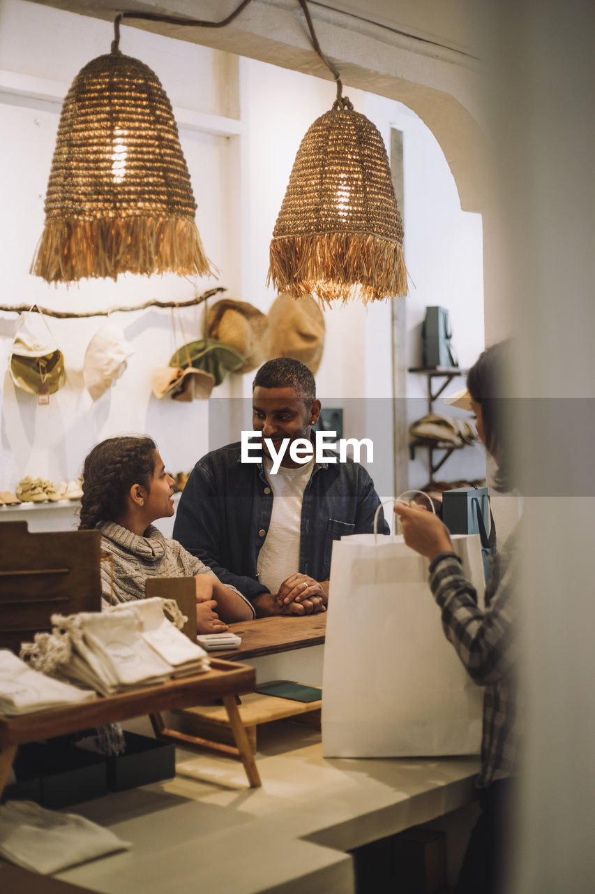 Father and daughter looking at each other while saleswoman packing bag in store