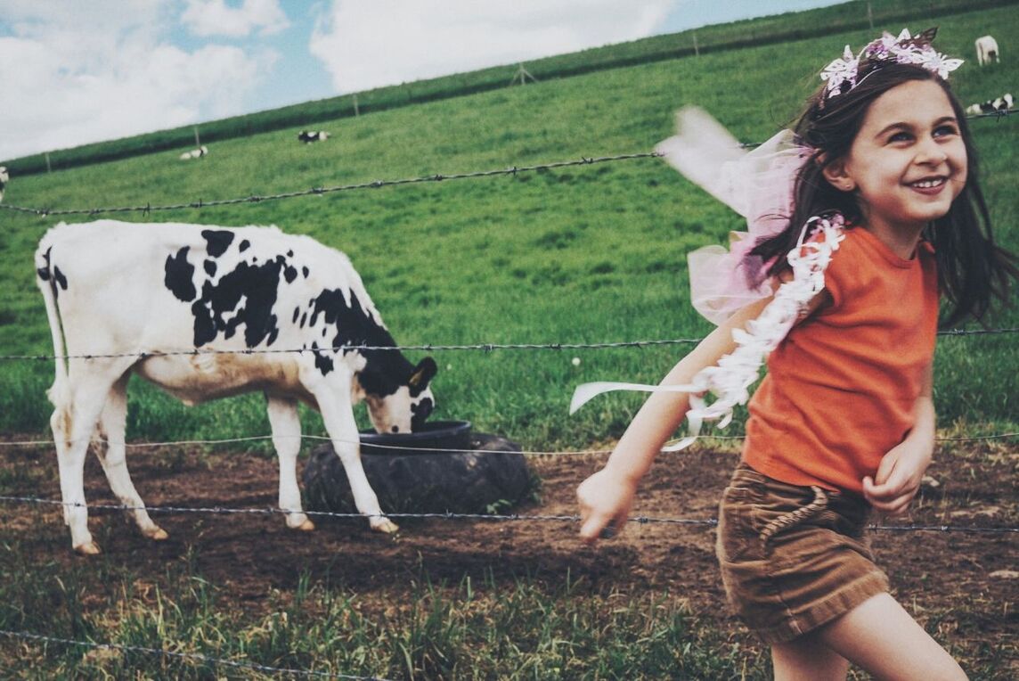 Side view of girl running on field against a cow