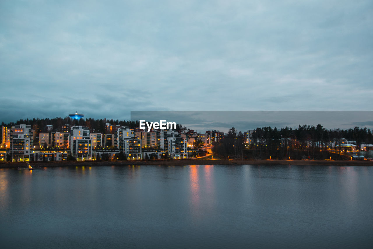 Buildings by river against sky in city