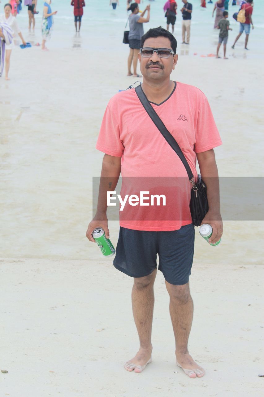 FULL LENGTH PORTRAIT OF YOUNG MAN STANDING ON BEACH