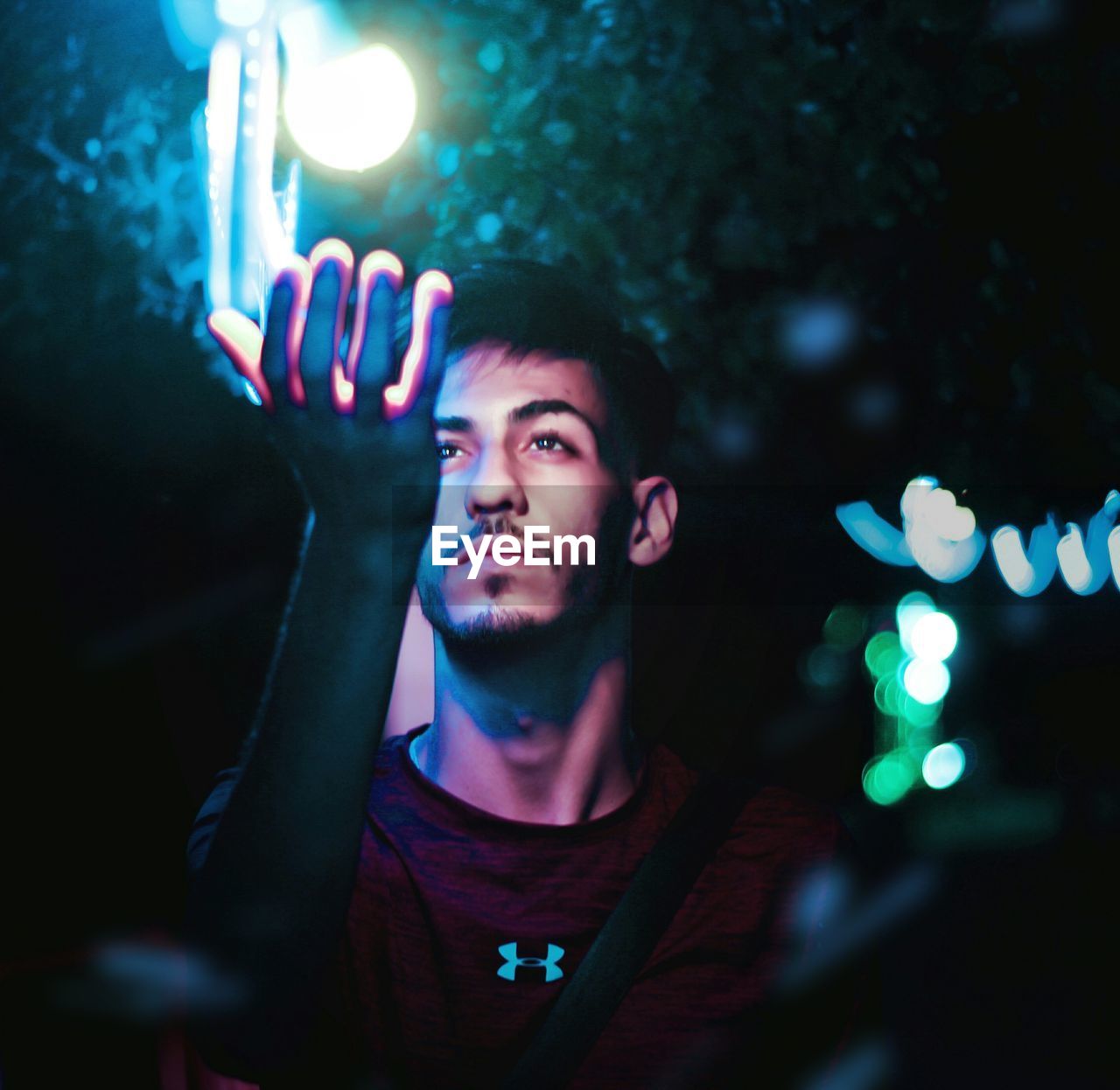 PORTRAIT OF YOUNG MAN LOOKING AT ILLUMINATED LIGHT