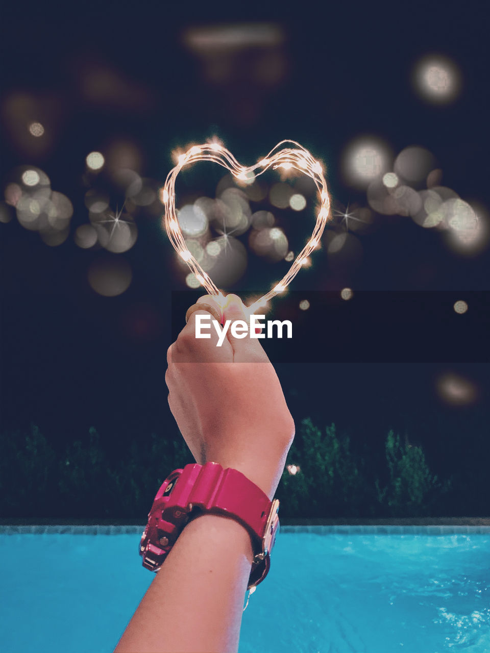 Cropped image of woman holding illuminated light in front of swimming pool at night