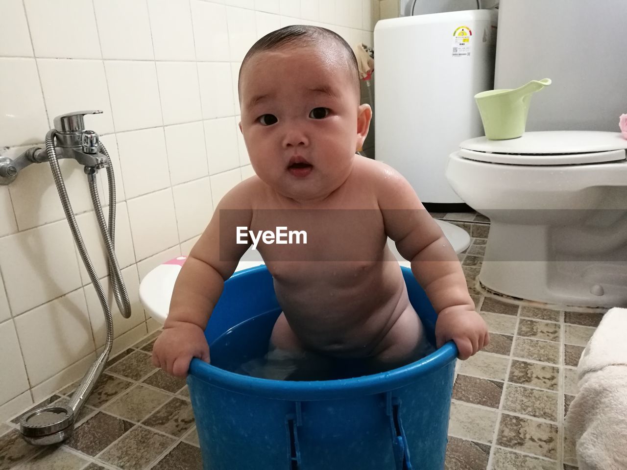 Portrait of cute baby boy standing in bucket at bathroom